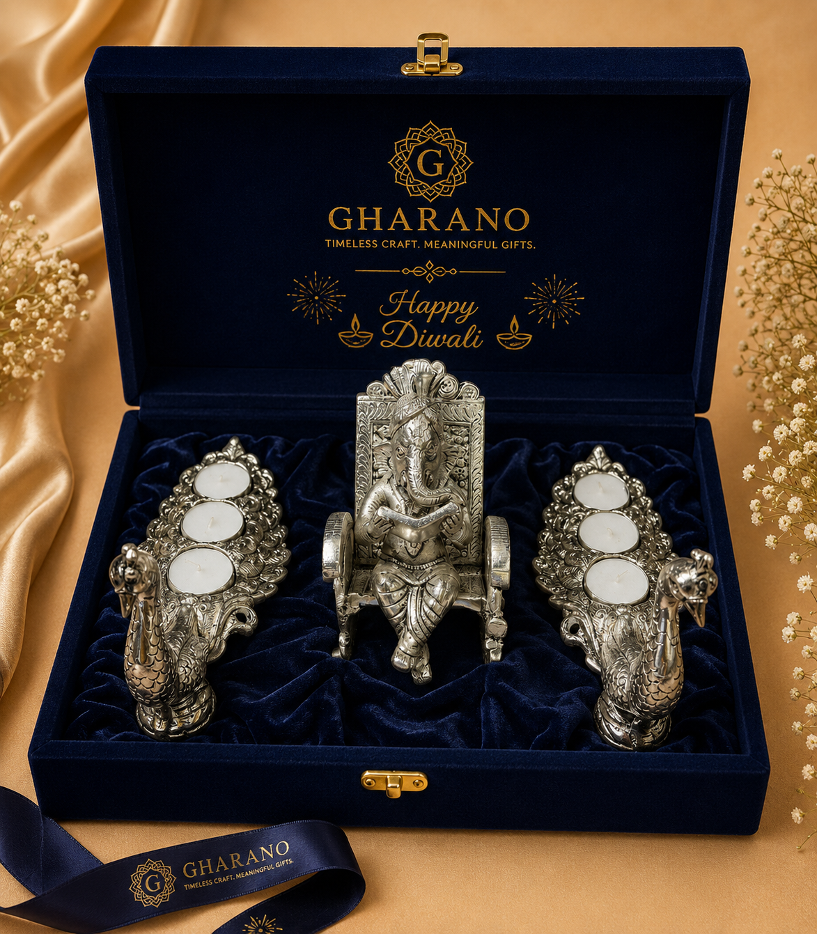 A Gharano Diwali gift set in an open navy velvet box with gold branding featuring a central silver Ganesha figurine and two german silver candle holders with T-lights.